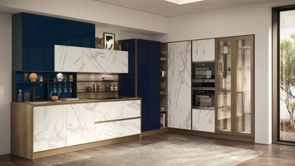 Cucina angolare Dafne Top di BEHOME con mobili effetto marmo bianco, pensili blu lucido, dettagli dorati e vetrina.