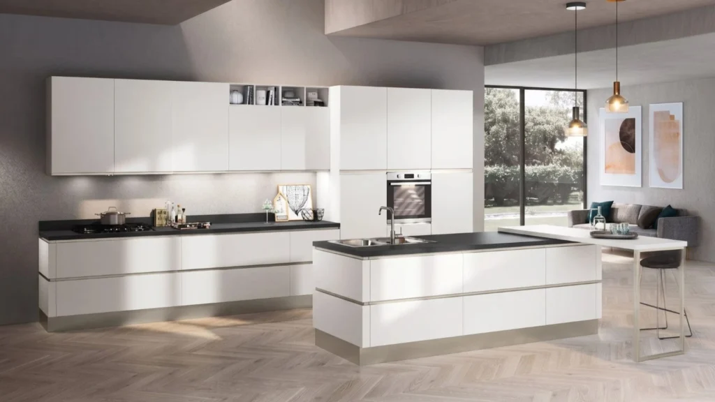 Cucina con isola Ines White di BEHOME: mobili bianchi, top scuro, penisola integrata e soggiorno sullo sfondo.