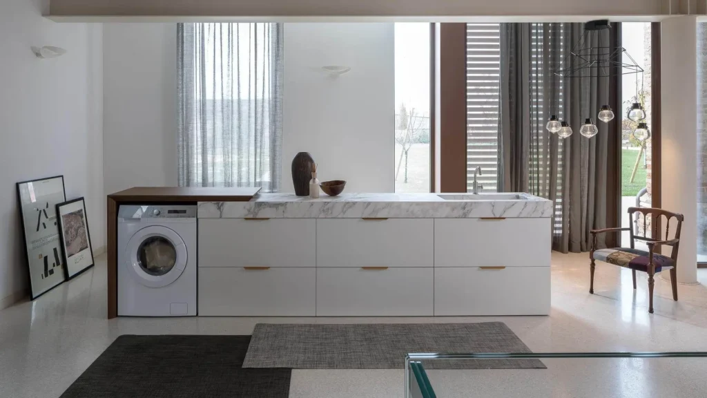 Mobile lavanderia Loren di BEHOME bianco con top effetto marmo, lavabo e vano lavatrice in legno.